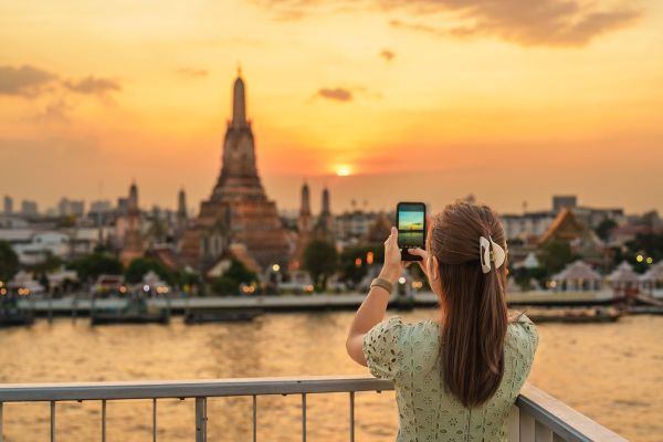 A tourist photographs a view of Wat Arun Temple from a rooftop bar.