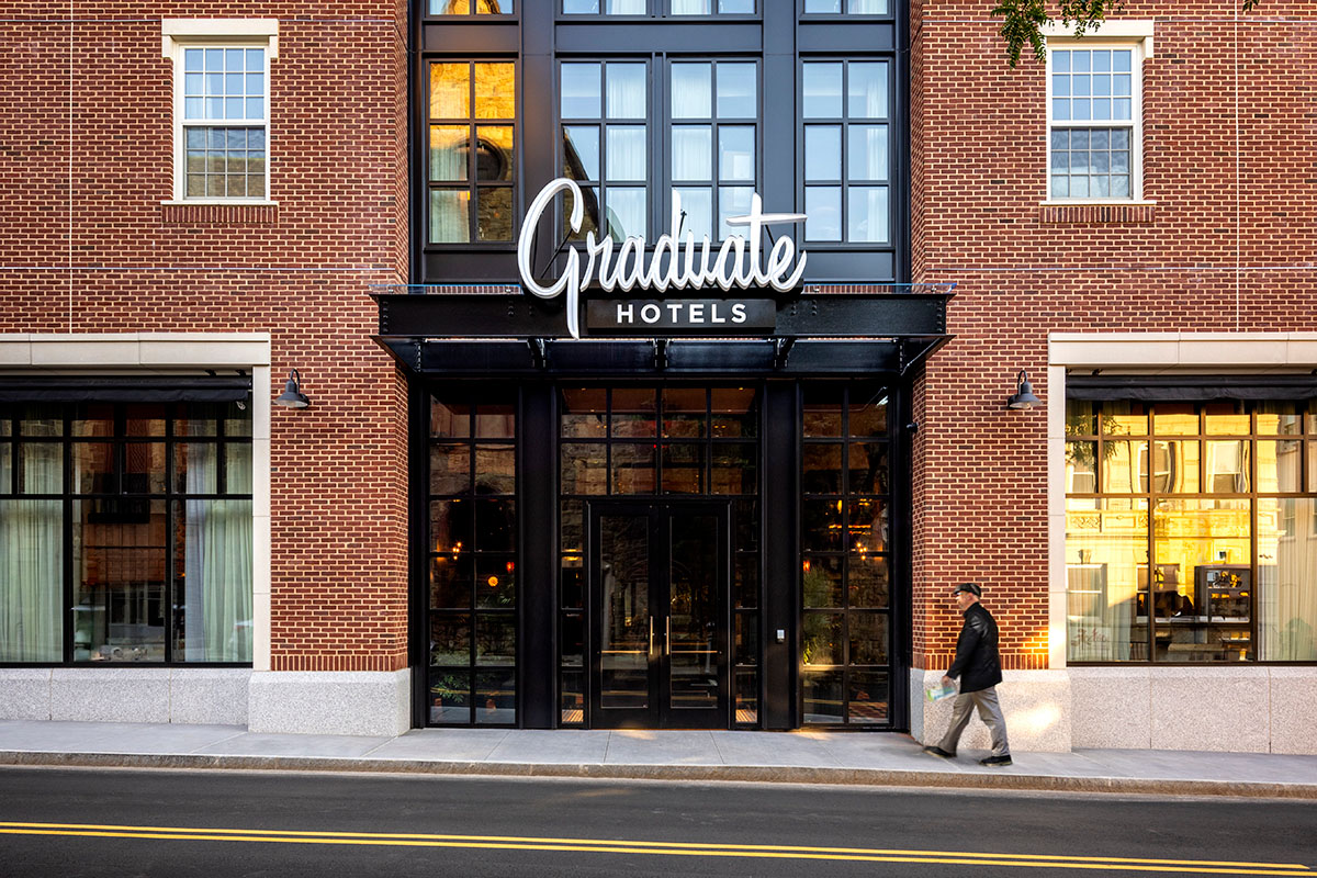 Exterior of a red brick hotel with a man walking along a sidewalk