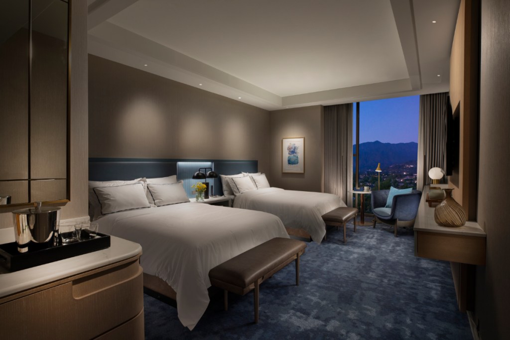 Image of a double room Hilton hotel guest room, scene from the inside with a dusky view of the skyline outside the window.