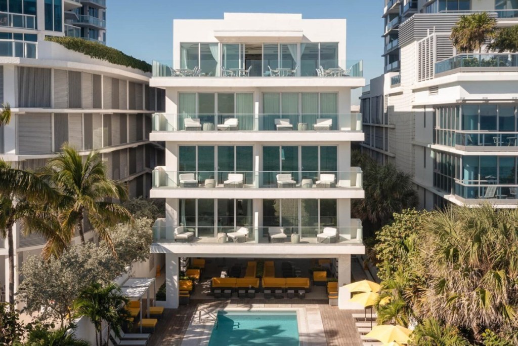 a glam resort in Miami Beach viewed from the outside on a sunny day with palm trees and deck chairs